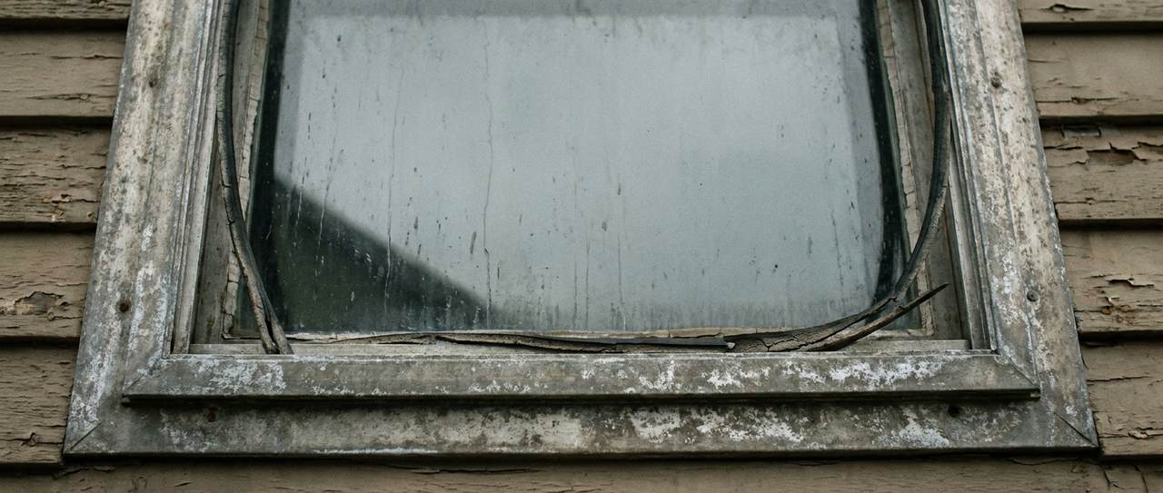 Close-up of an old aluminum-frame single-pane window with worn weatherstripping